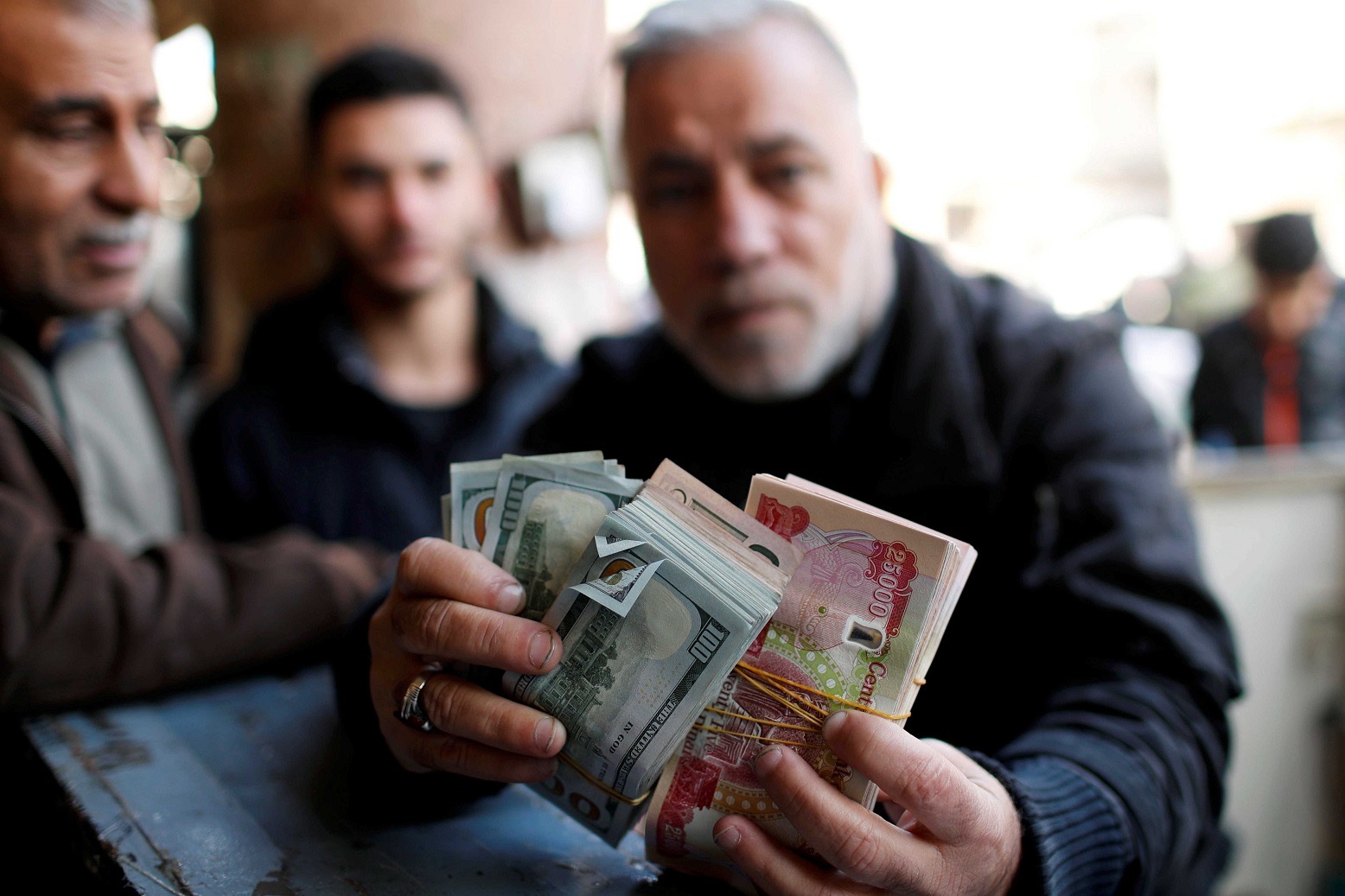 A man holds money as he poses for a picture at a foreign currency exchange market in Baghdad